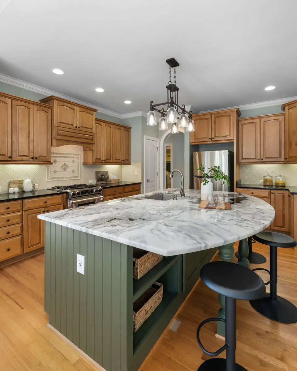 Kitchen with a sage green island, white stone counters and a black pendant light